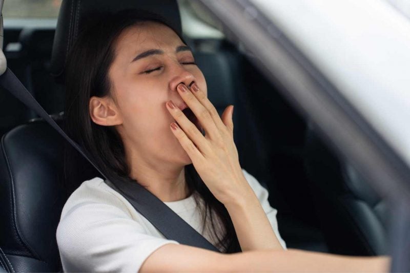 A young Asian woman yawns while she's driving.