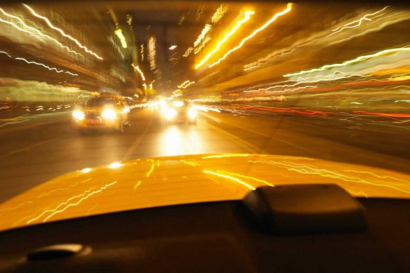Light flares on a car windshield while driving at night, on a busy road.