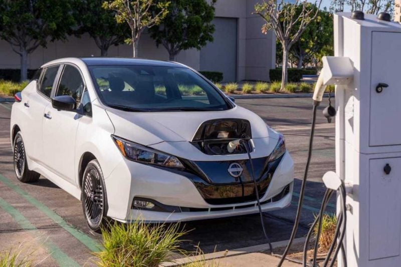 A white Nissan LEAF EV vehicle is charging at a charging station.