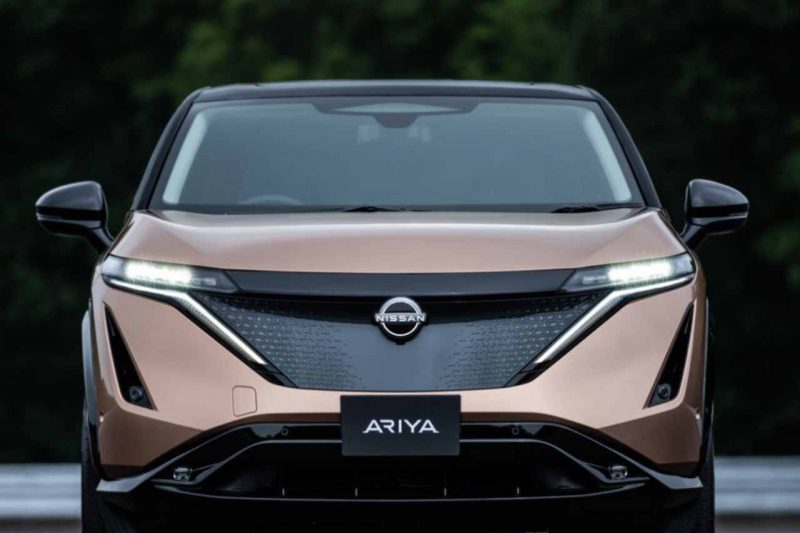 The exterior of a brown Nissan Ariya vehicle has its headlights on.