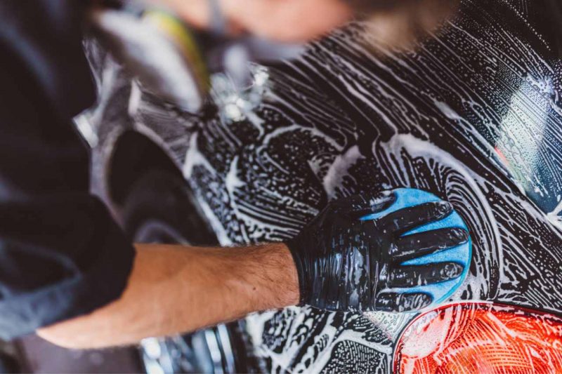 A car technician cleans the exterior of a vehicle, performing a car detailing service.