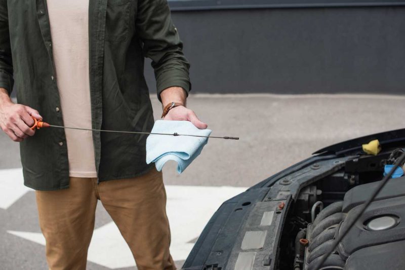 A Caucasian man uses a dipstick to check the transmission fluid on his vehicle.