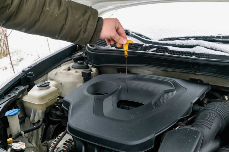 A man checking his engine oil dipstick under the hood of his vehicle.