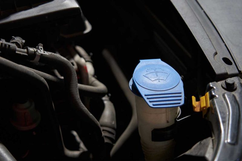 A close-up shot of the car's engine bay showing a washer fluid reservoir with a blue cap. One of our 5 tips to maintain your vehicle is to make sure you have new windshield wipers and your washer fluid is topped up!