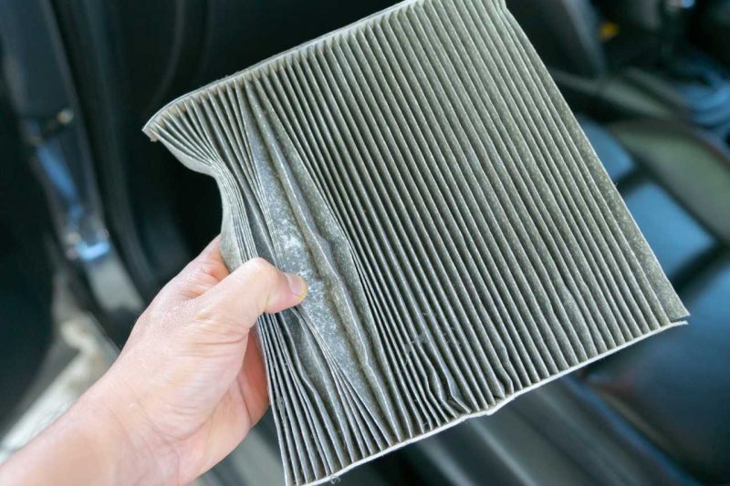 A man holding up a dirty cabin air filter during a car service appointment. It's recommended to change air filters as part of our 5 tips to maintain your vehicle.