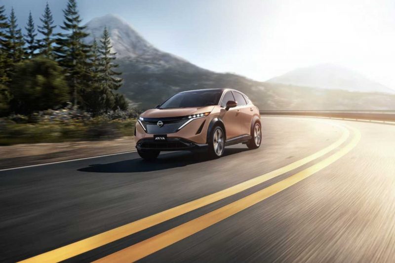 The Ariya SUV is driven down a sunny highway with mountains in the background.