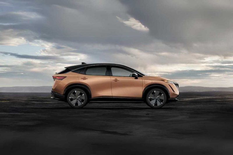 The Nissan Ariya electric vehicle is parked outdoors, with a moody sky above.
