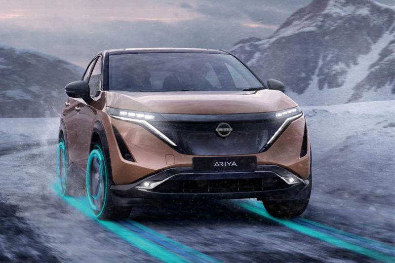 The Nissan Ariya drives down a snowy highway in the mountains, using the Snow Drive Mode.