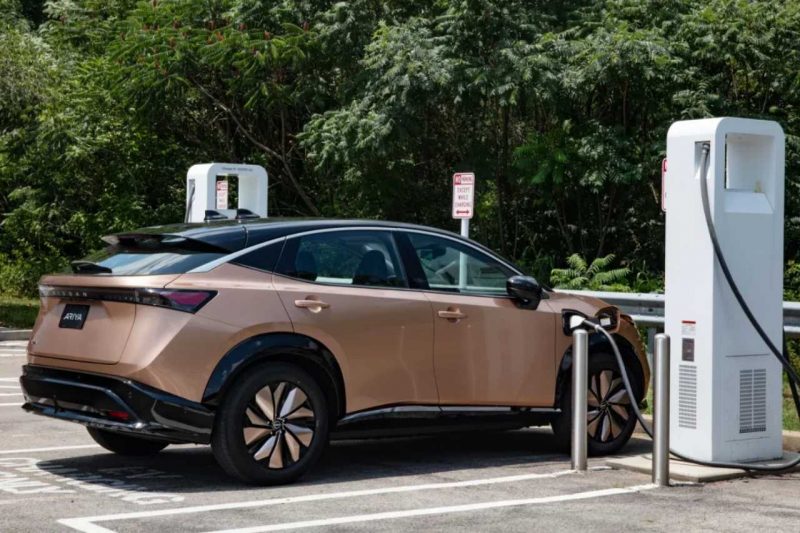 The 2024 Nissan Ariya is parked at a public charging system for electric vehicles on a sunny afternoon.