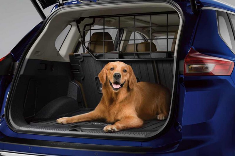 A dog sits in the back of a Nissan Rogue SUV, using the retractable pet divider accessory.