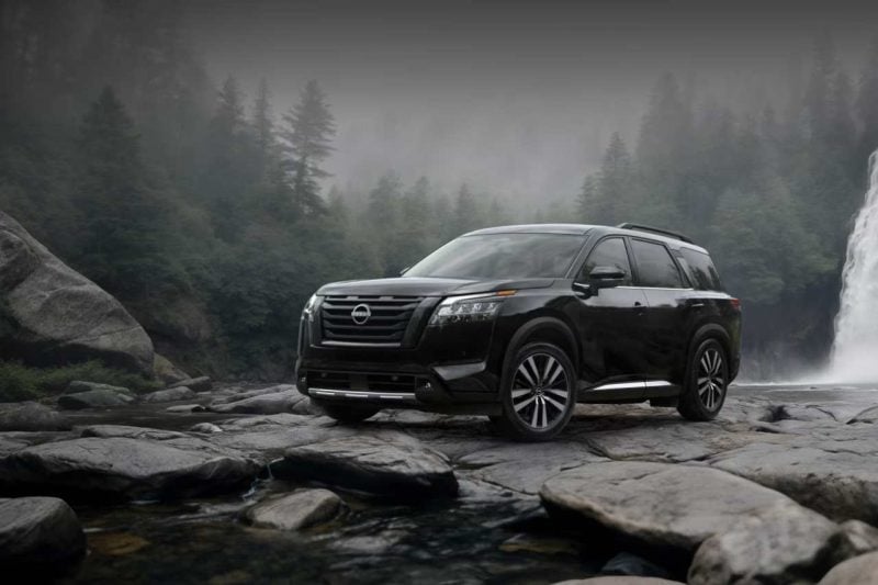 The 2024 Nissan Pathfinder in black is posed on black rocks in front of a moody forest.