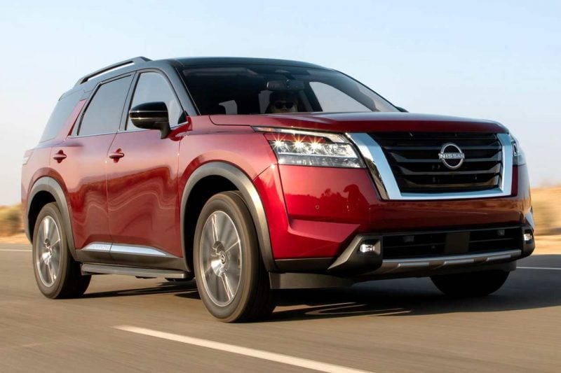 A red 2024 Nissan Pathfinder SUV drives down a sunny highway.