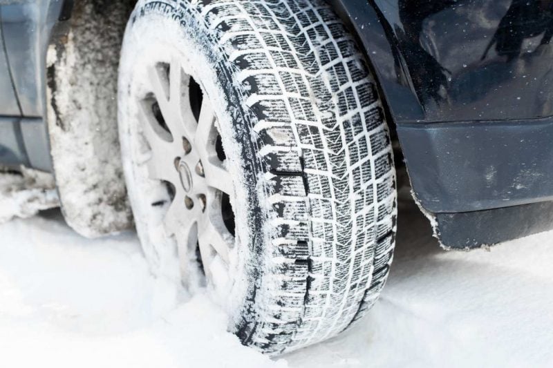 A close-up of winter tires on a vehicle driving through the snow.