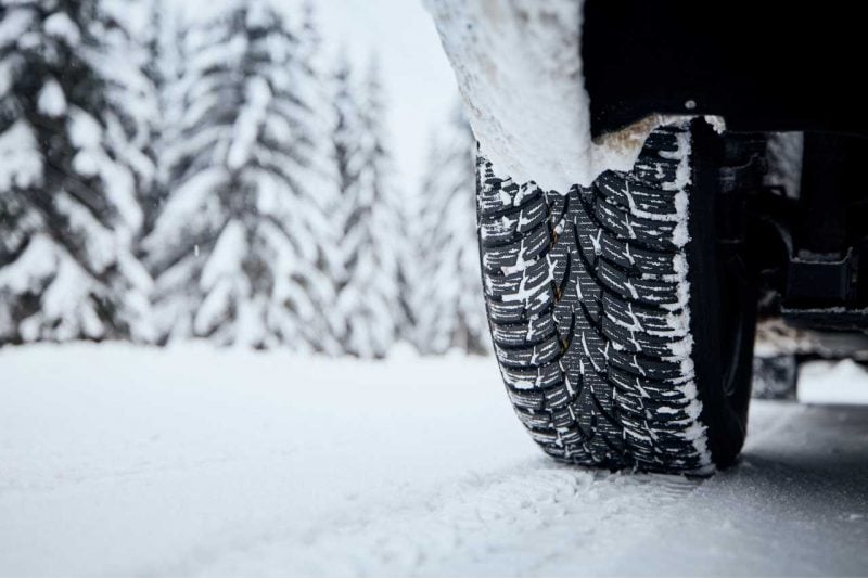 A vehicle drives through the snow on a forest road, and has snow in its winter tires.