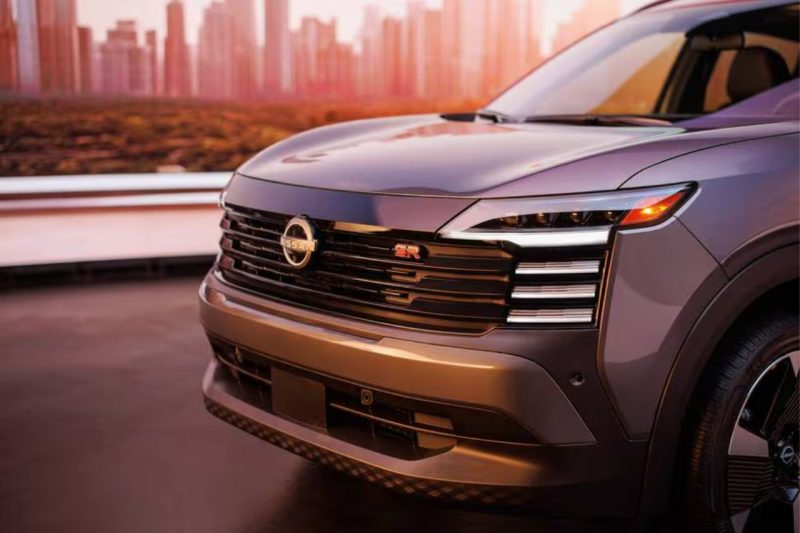 The new Nissan Kicks front grille and hood posed in front of a cityscape at sunset.