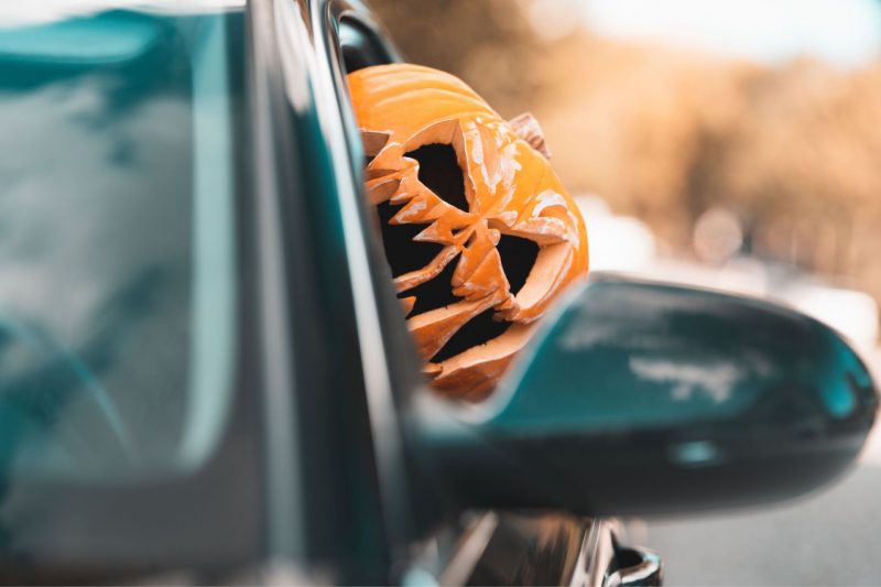 A person wearing a Jack-o-Lantern pumpkin drives a car. The blog post explains spooky car service issues for Halloween.