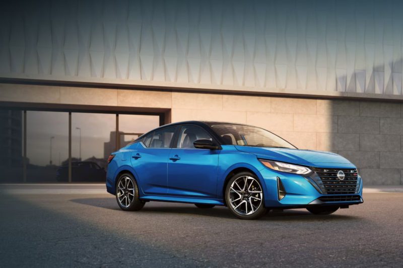 The new 2025 Nissan Sentra sedan in blue is parked outside a modern building at sunset.