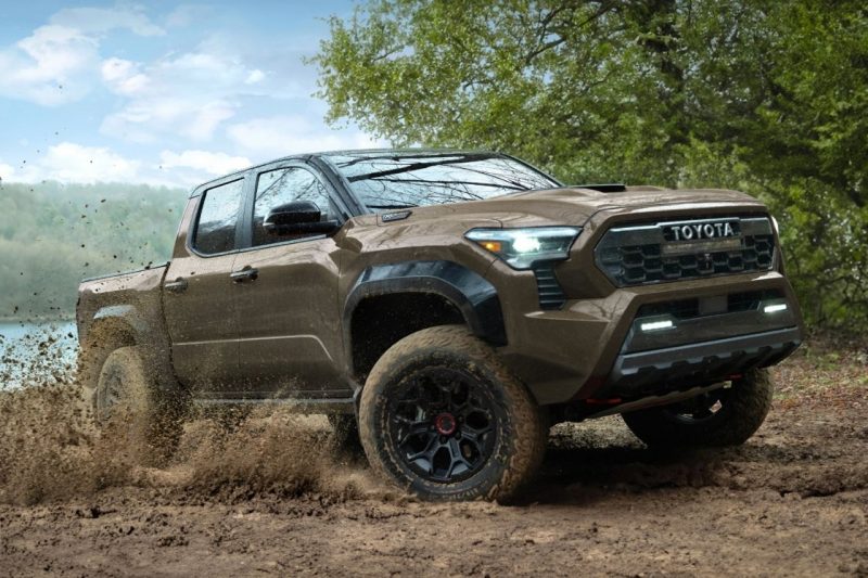 A brown Toyota truck drives through a large puddle of mud on a sunny day.