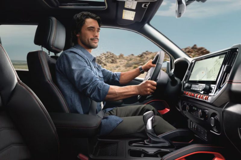 A Caucasian dark-haired man drives a Nissan truck, sitting in the comfortable cab and holding the steering wheel.