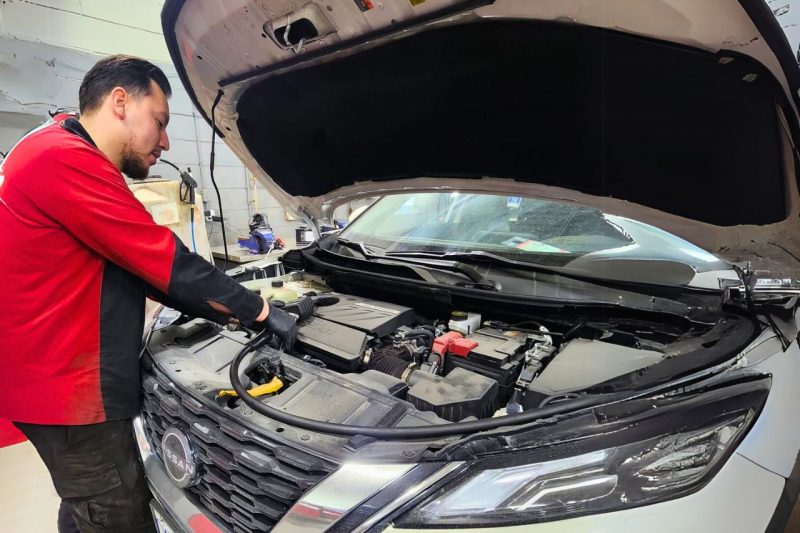 A Nissan service technician looks under the hood of a car to refill engine oil.