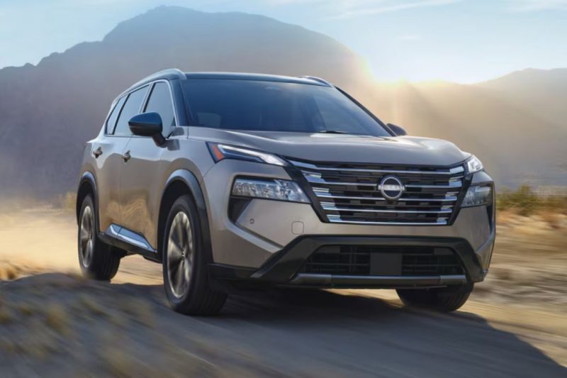 The 2025 Nissan Rogue in a champagne colour drives down a dusty road with mountains in the far distance.