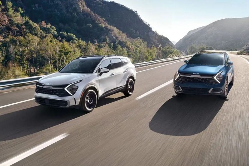 Two Kia Sportage SUVs drive down a sunny highway.