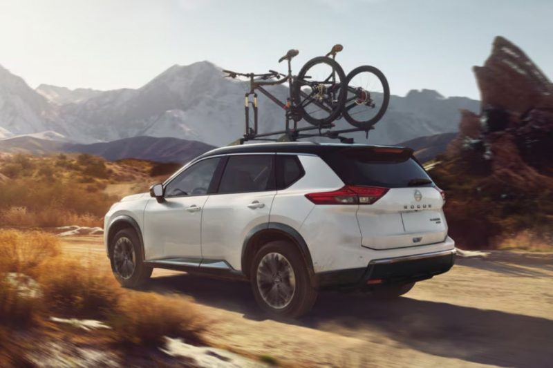 A white Nissan Rogue SUV drives down a mountain road with sports bikes on top.