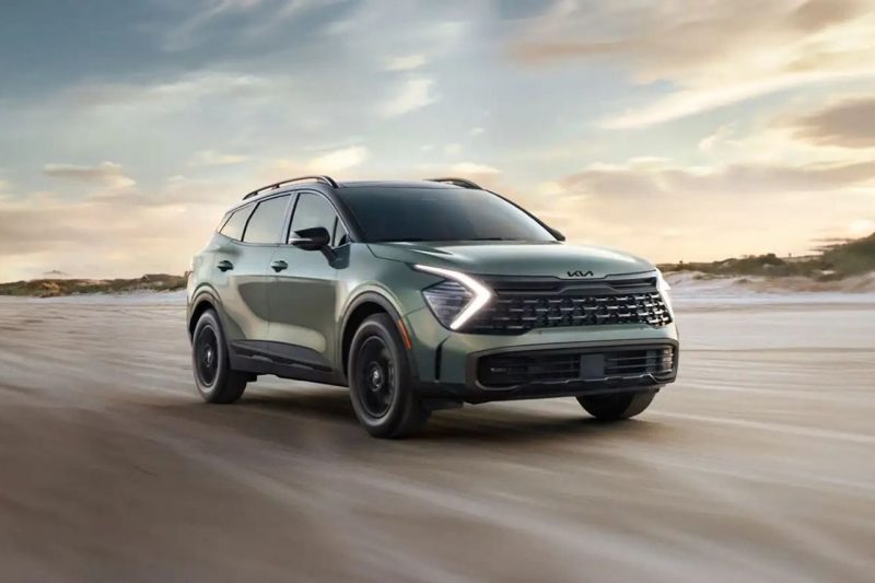 A green Kia Sportage SUV drives down a beach in low lighting.
