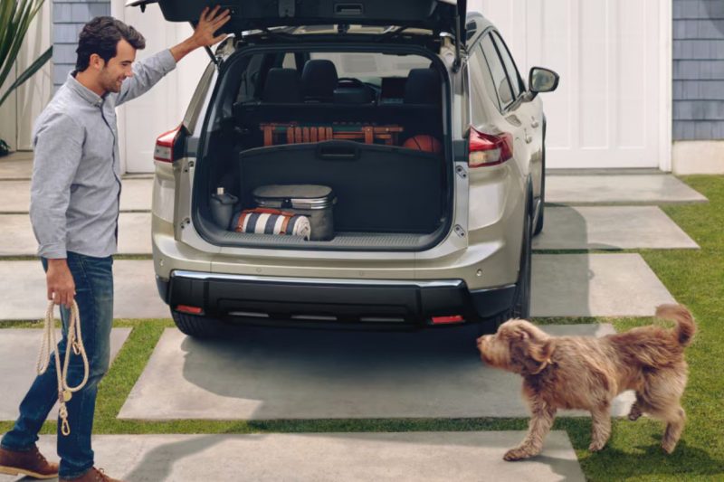 A Caucasian man opens the trunk of his Nissan Rogue to allow his dog to climb in.